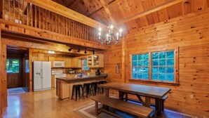 A spacious wooden cabin with a large dining table, kitchen area, and a balcony.