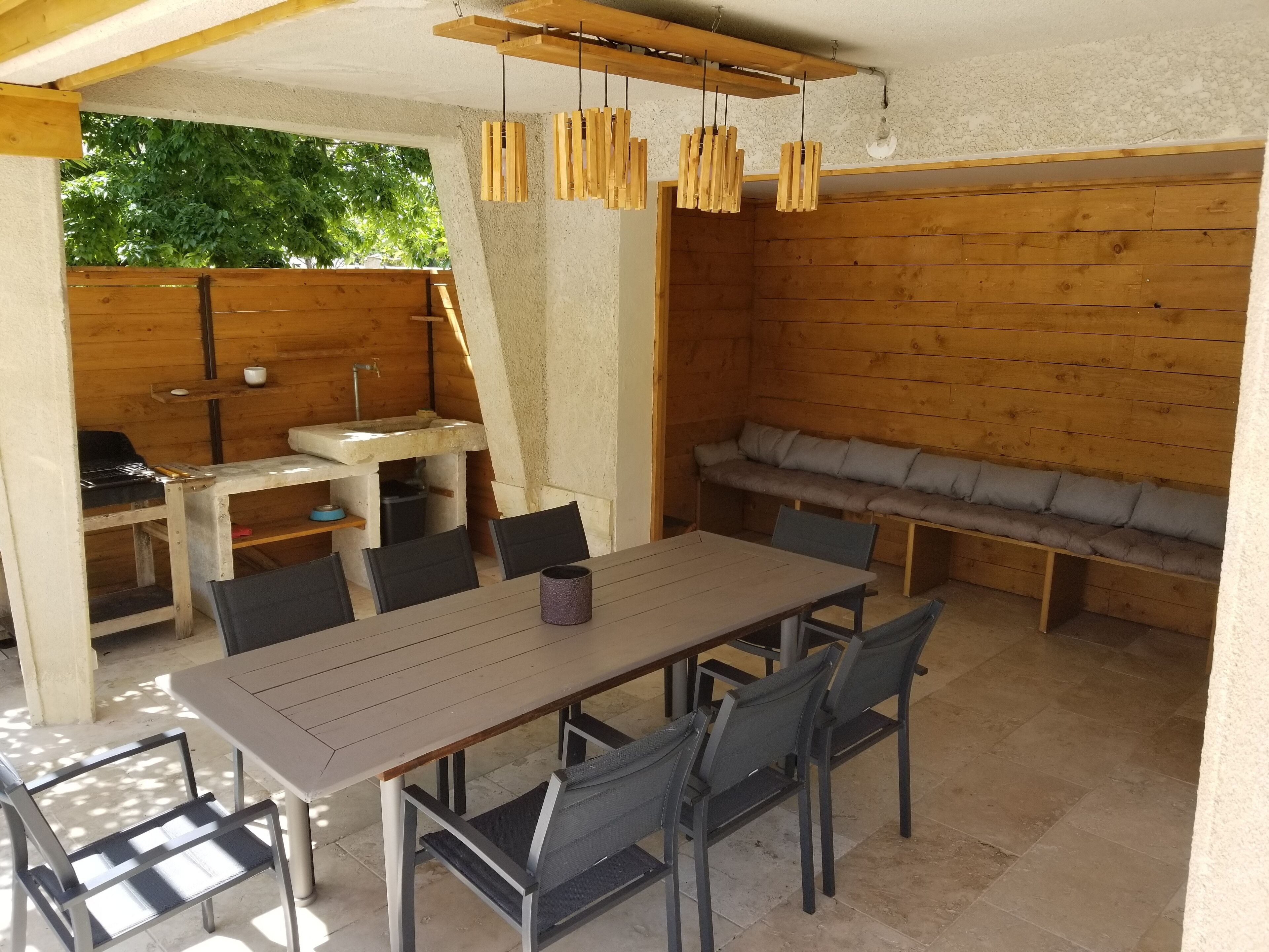 An outdoor dining area with a table and chairs, a wooden bench, and hanging wooden light fixtures.