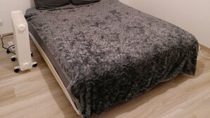 A small, neatly made bed with a grey textured blanket and two dark pillows. A white radiator is positioned to the left of the bed. - Chambre parquet flottant (Savigné-lʼÉvêque)