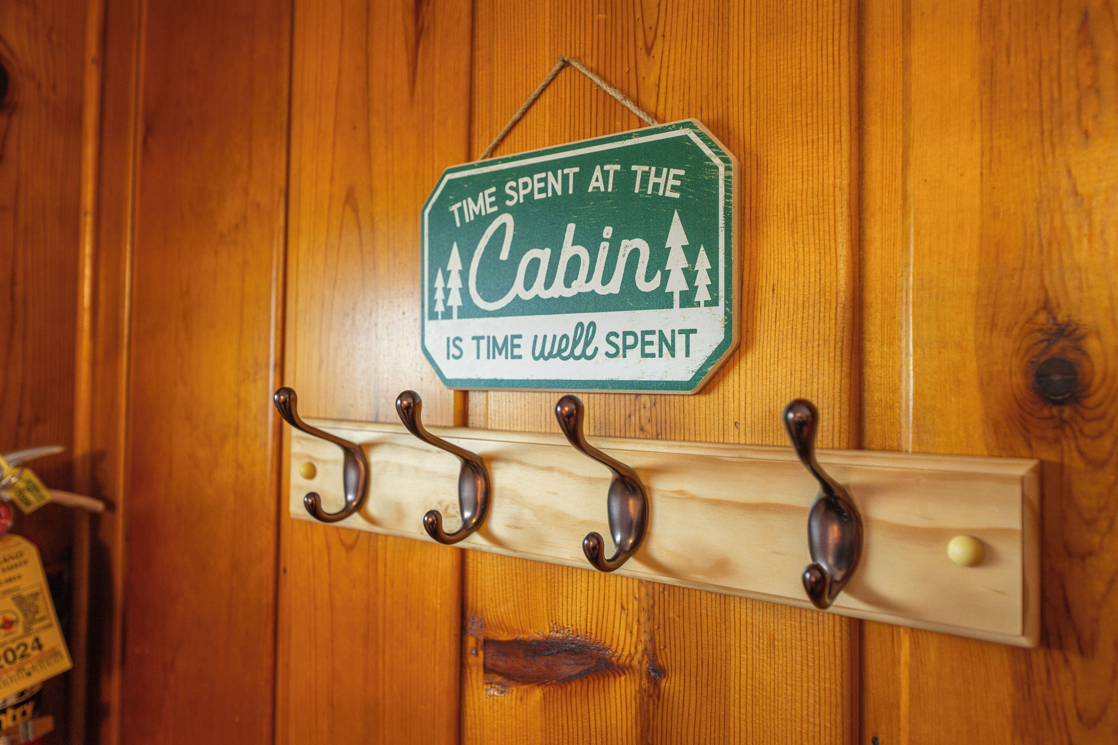 Een houten cabin-deur met een bordje waarop staat 'Tijd doorgebracht in de cabin is tijd goed besteed' en een kapstok met haken.