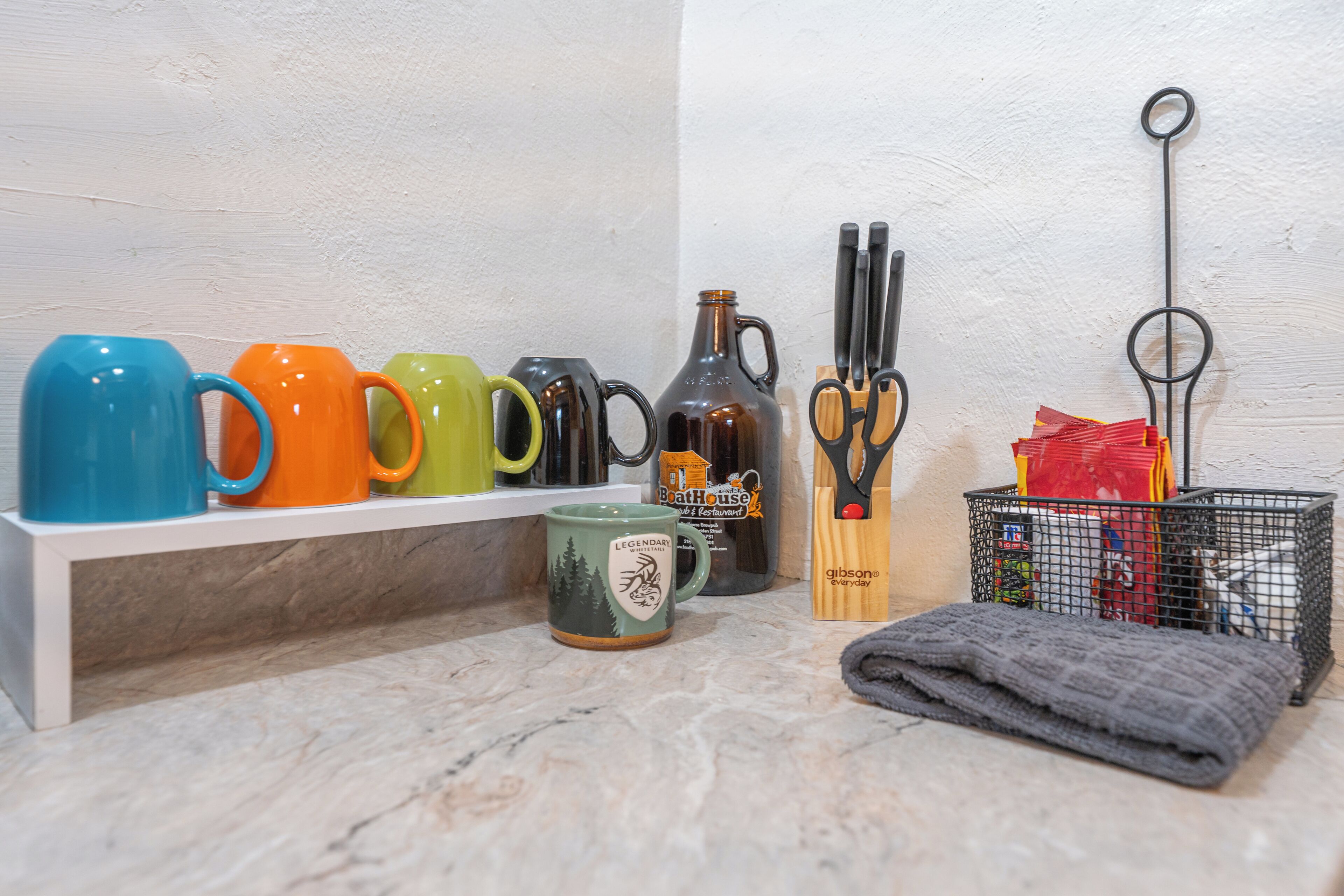 Una estant plena de tasses de colors, una ampolla i utensilis de cuina.