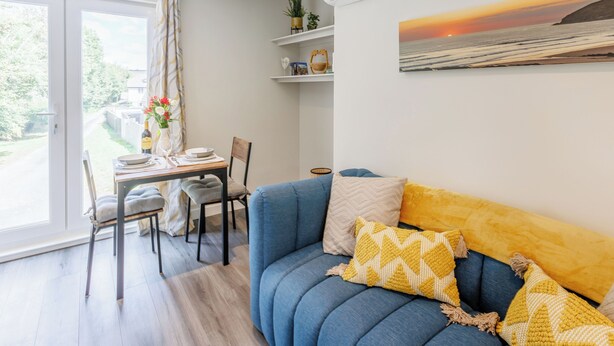 Un salon moderne avec un canapé bleu, une table à manger et des chaises, ainsi qu’une grande fenêtre.