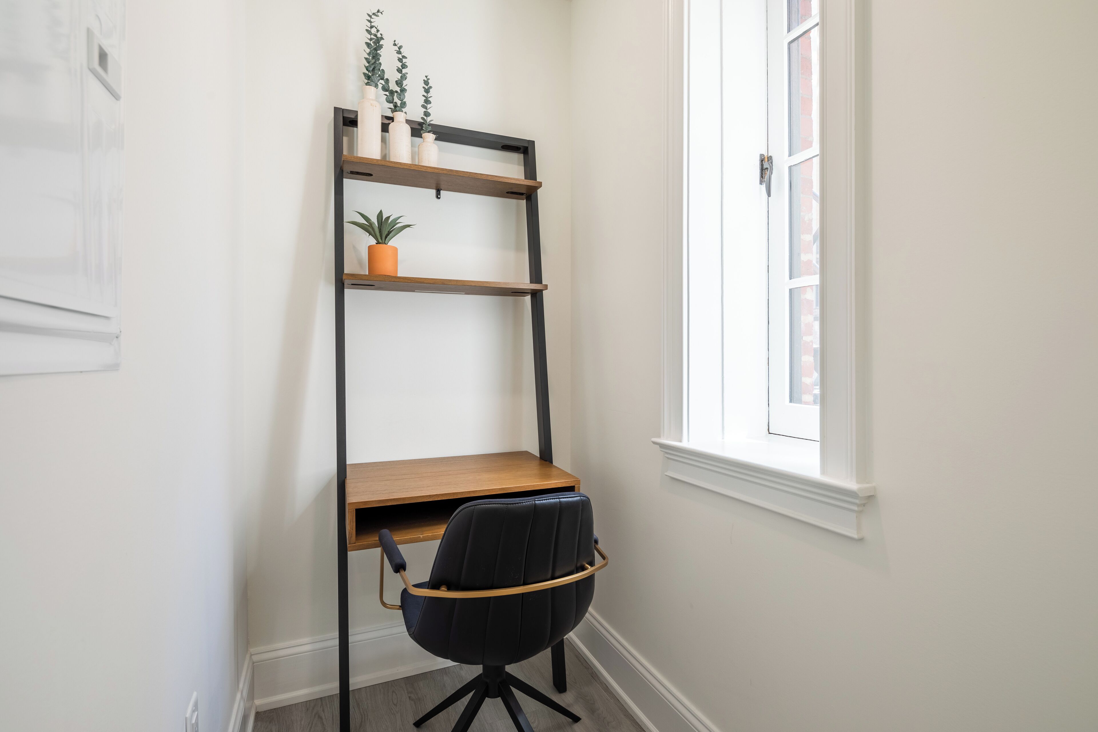 A corner office with a desk, chair, and a black shelving unit against a white wall.