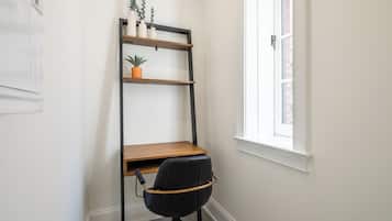 A corner office with a desk, chair, and a black shelving unit against a white wall.