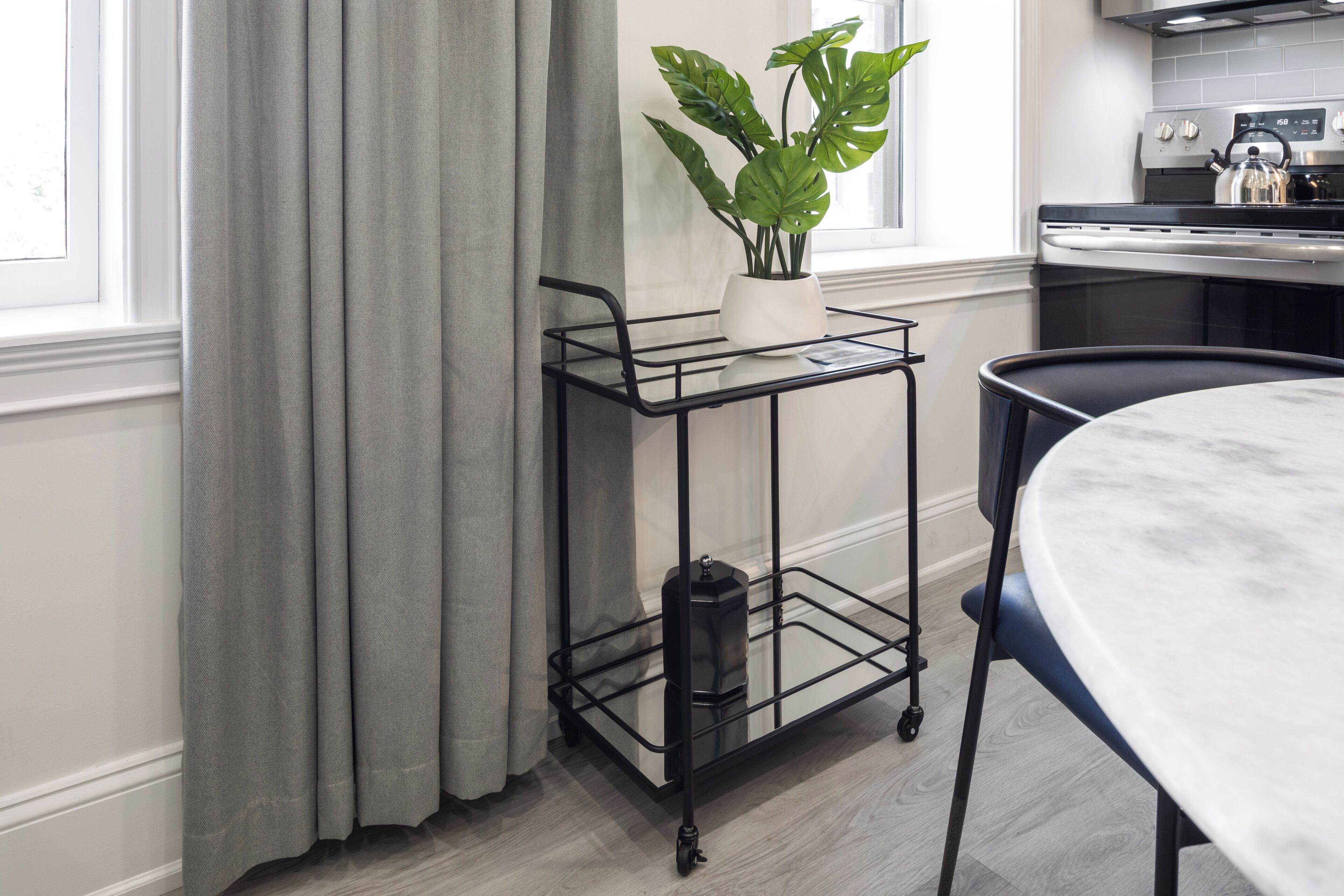 A kitchen with a round table, a metal cart with a potted plant, and a stove.