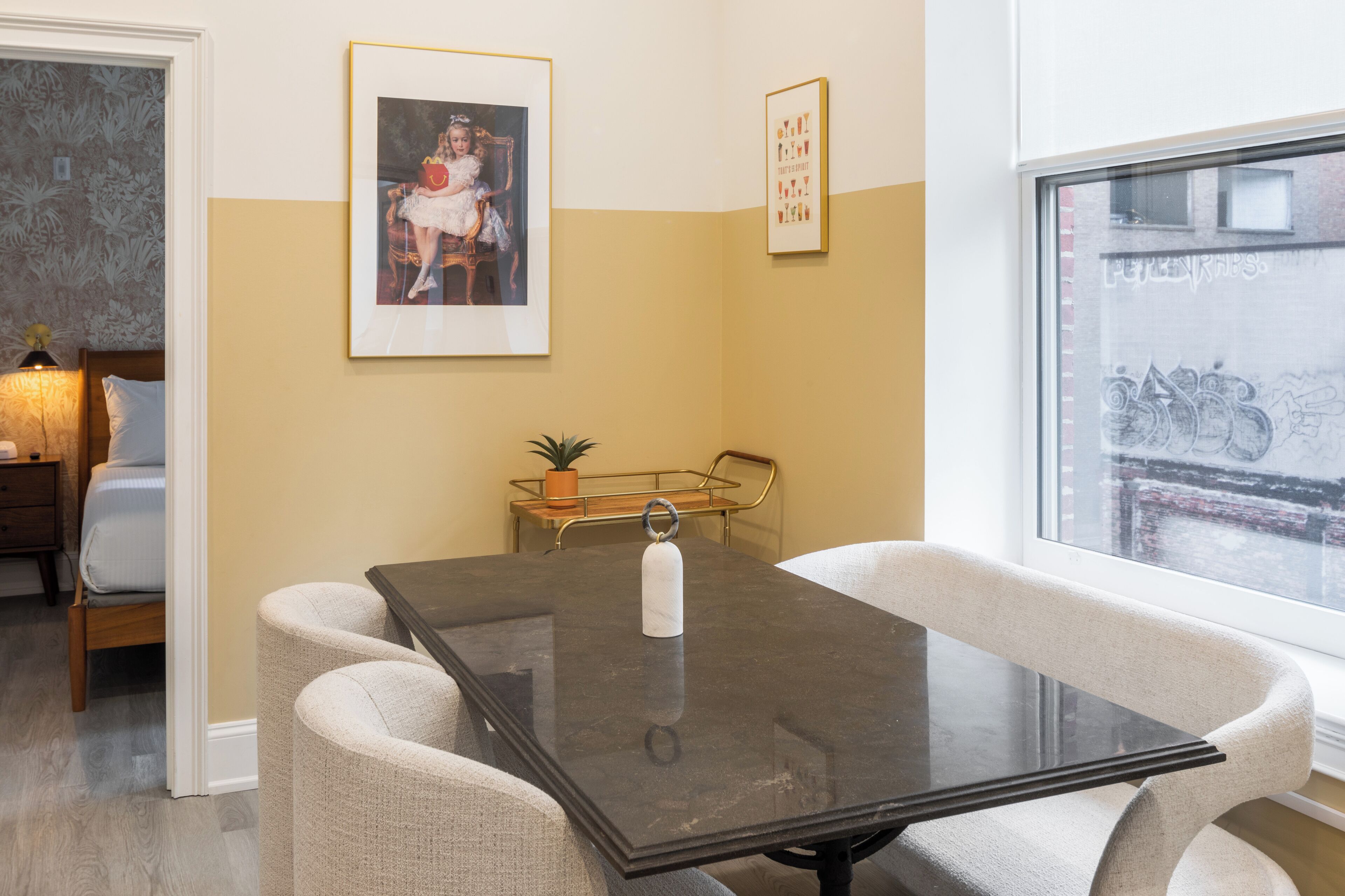 A dining area with a glass-top table, cushioned chairs, a framed picture on the wall, and a view of the outside through a window.