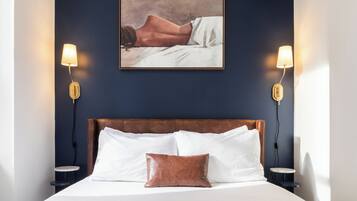 Een slaapkamer met een groot bed, twee bedlampen, een gekaderd kunstwerk boven het bed en een klein tafeltje naast het bed.