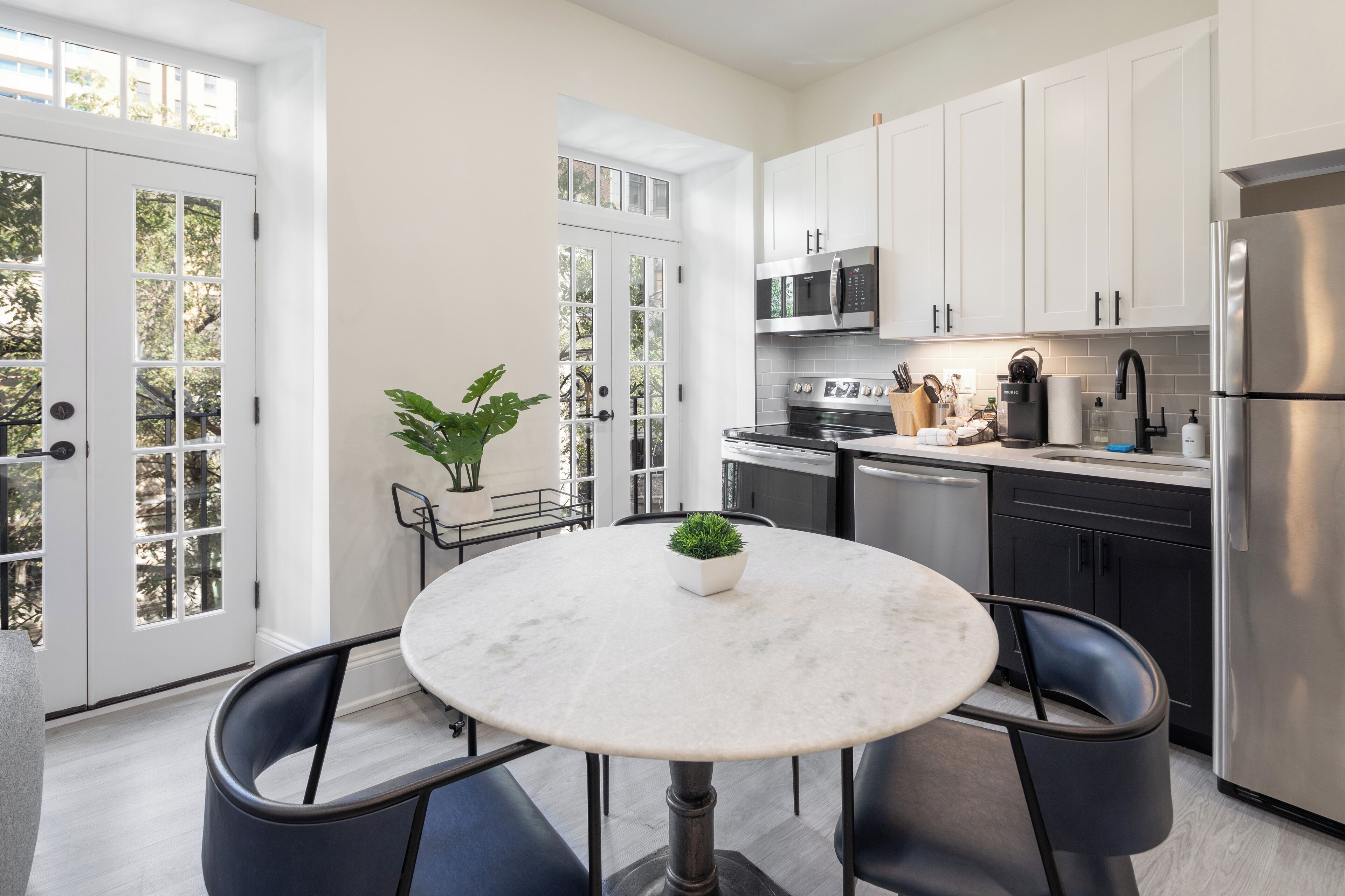 Una cocina moderna con armarios blancos, electrodomésticos de acero inoxidable y una mesa redonda de mármol con dos sillas.