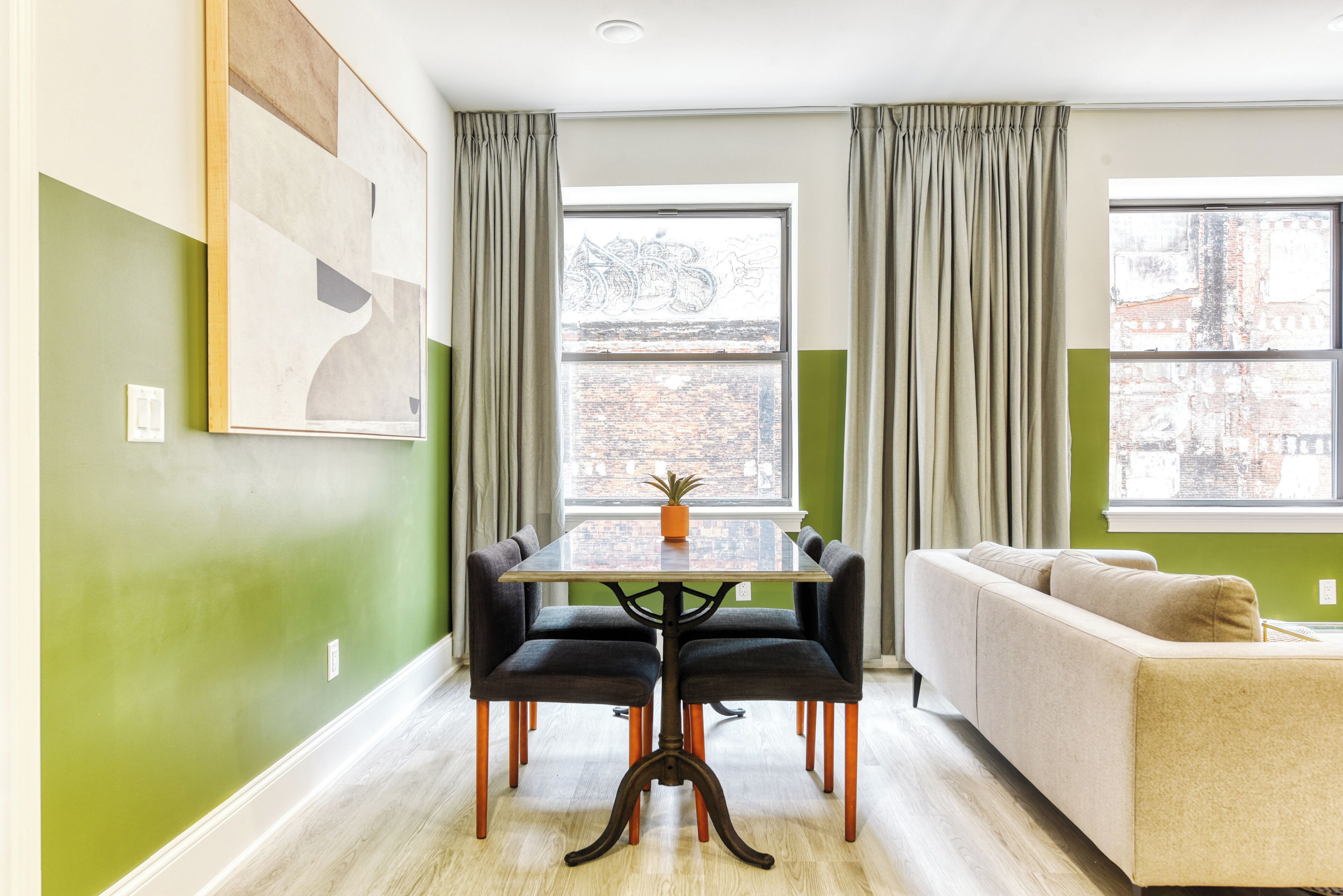 Uma área de refeições com mesa e cadeiras, um sofá e uma janela com cortinas.