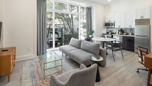 A modern living room with a grey sofa, a glass coffee table, and a dining area with a small round table and chairs.