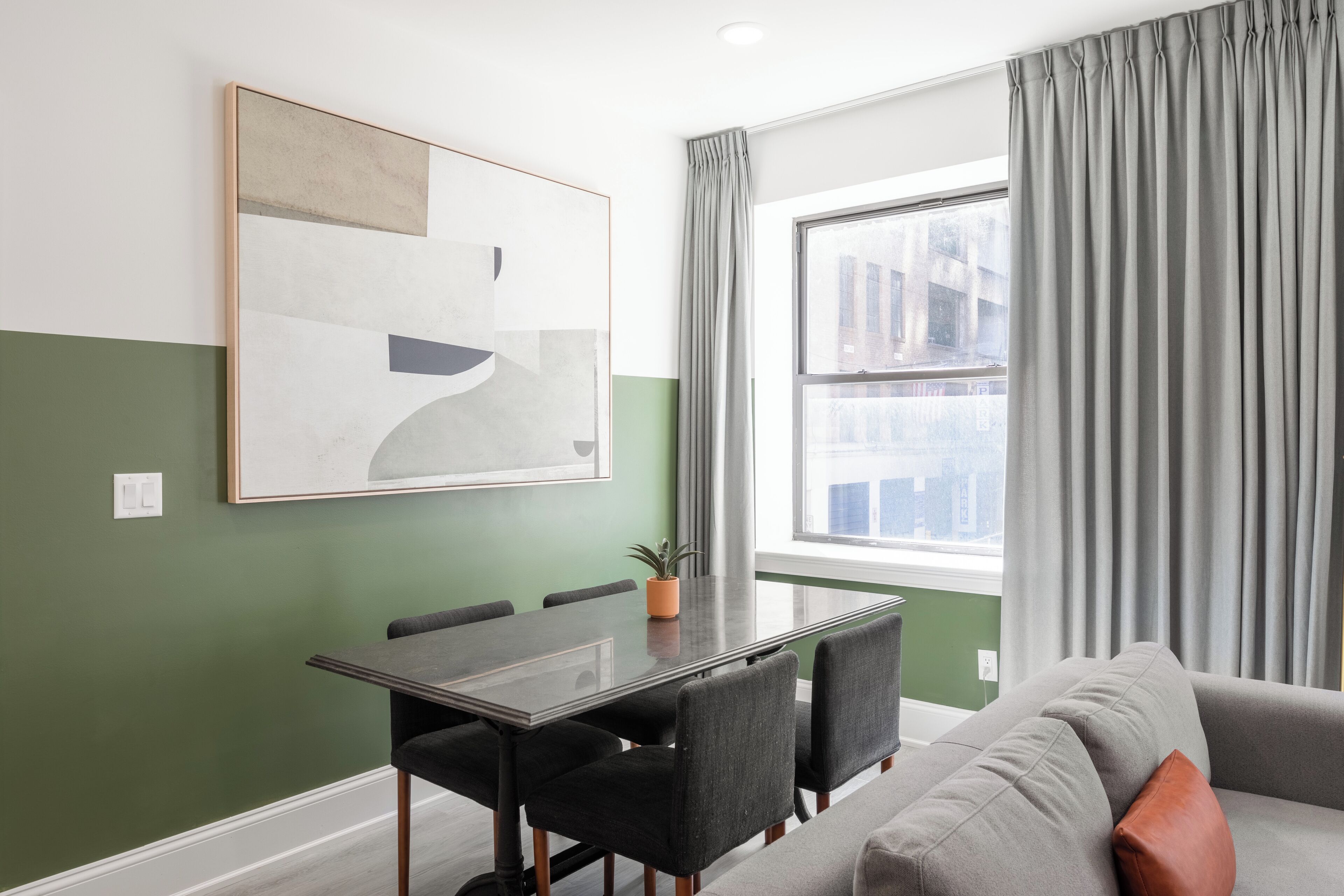 Una sala de estar moderna con una mesa de comedor, sillas, un sofá y un cuadro abstracto grande en la pared.