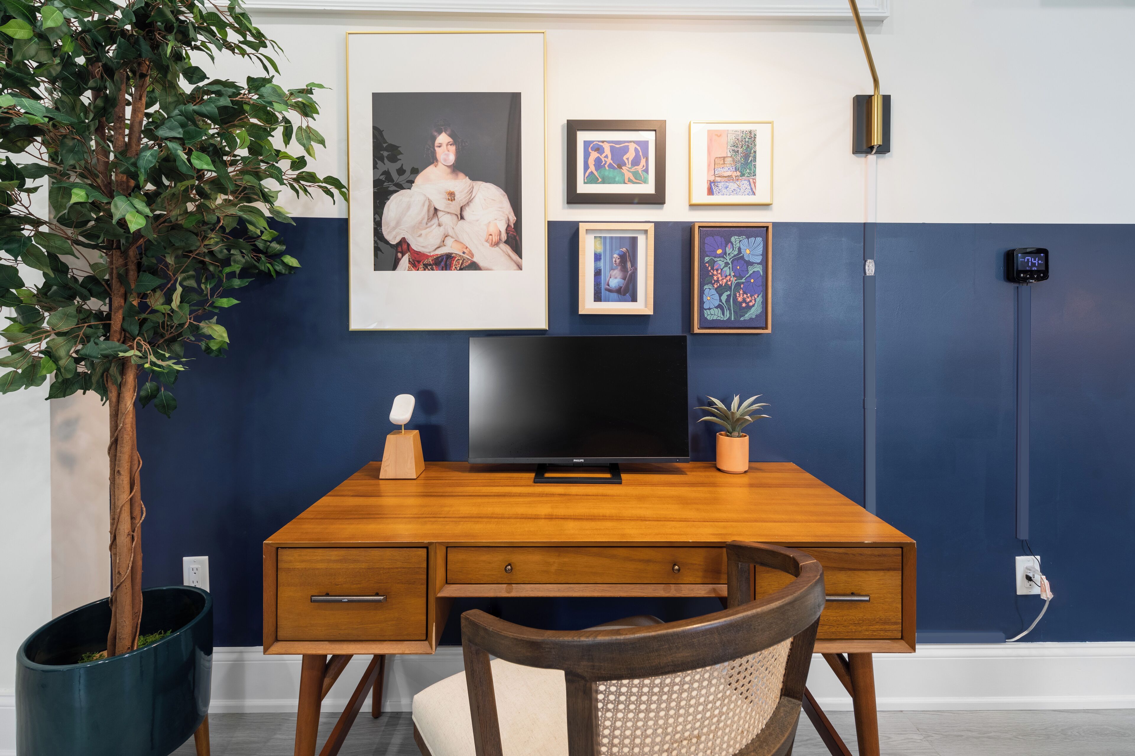 Une chambre moderne avec un bureau en bois, une télévision et des œuvres d’art encadrées accrochées au mur.