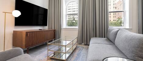 Un salon moderne avec un téléviseur à écran plat, une table basse en verre, un canapé gris et un meuble en bois.