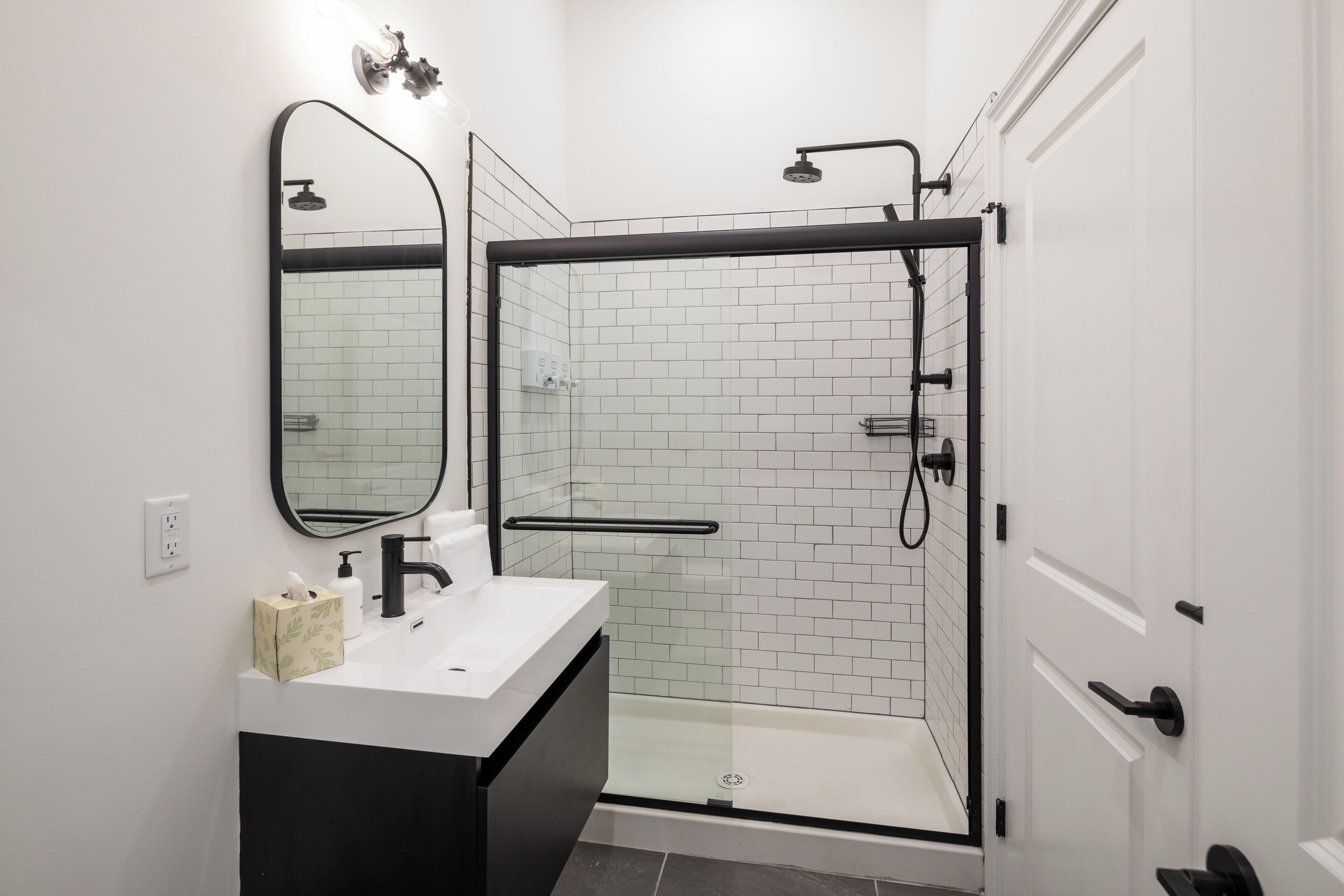 A modern bathroom with a glass-enclosed shower, a white sink with a black cabinet, and a mirror above the sink.