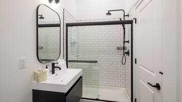 A modern bathroom with a glass-enclosed shower, a white sink with a black cabinet, and a mirror above the sink.