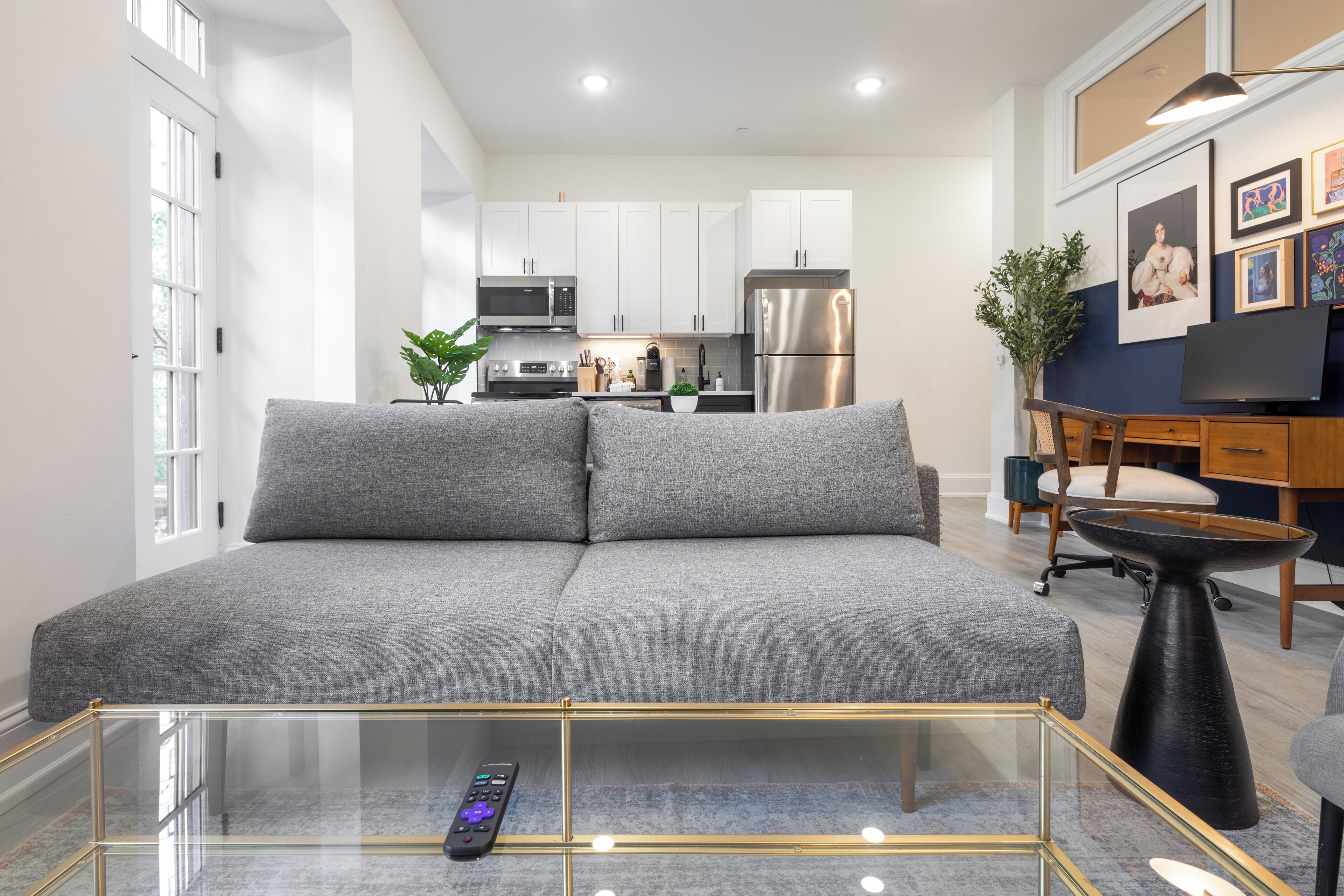 A modern living room with a grey sofa, a glass coffee table, and a remote control on it.