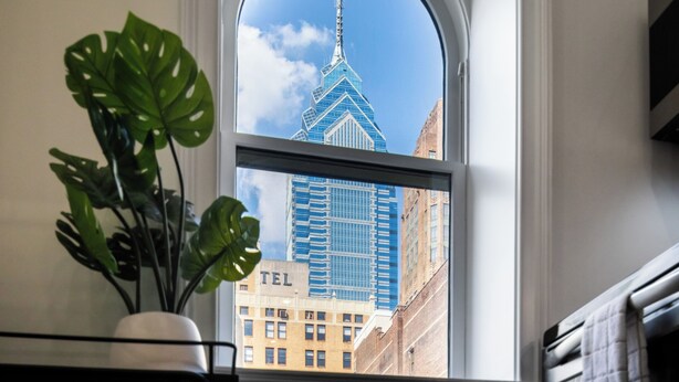 A view through a window of a building with a distinctive spire, a plant on the windowsill, and a visible 'TEL' sign on a building below.