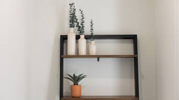 A black metal shelf unit with three white ceramic vases and a potted plant on the top shelf, and a single potted plant on the bottom shelf.