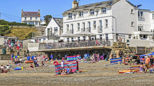 A coastal building with a balcony overlooking the beach, surrounded by beachgoers and beach umbrellas. - 2 bedroom accommodation in Aberdaron (Aberdaron)