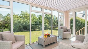 A spacious sunroom with large glass doors, wicker furniture, and a fruit bowl on a coffee table. - 2 bedroom accommodation in Aberdaron (Aberdaron)