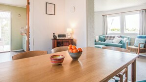 A dining area with a wooden table, a colorful bowl, and a bowl of oranges. There is a blue sofa with cushions in the background. - 2 bedroom accommodation in Aberdaron (Aberdaron)