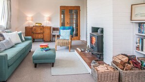 A cozy living room with a sofa, a chair, a wooden cabinet, a fireplace, and a bookshelf. - 2 bedroom accommodation in Aberdaron (Aberdaron)