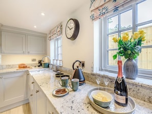 A kitchen with a clock, a window with yellow roses, and a bottle of Bollinger Rose wine on the counter. - 2 bedroom accommodation in Halton Holegate (Halton Holegate)