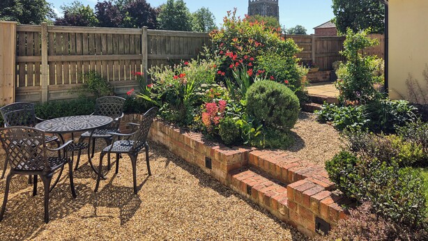 A patio with a brick wall, a wooden fence, and a garden with various plants and flowers. - 2 bedroom accommodation in Halton Holegate (Halton Holegate)