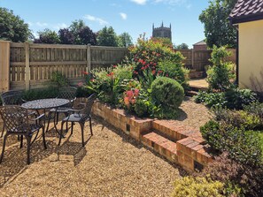 A patio with a brick wall, a wooden fence, and a garden with various plants and flowers. - 2 bedroom accommodation in Halton Holegate (Halton Holegate)