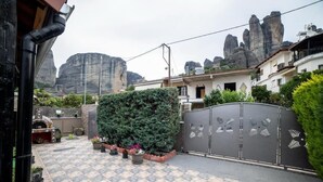 Un cortile con pavimento a scacchi, piante in vaso, un'alta siepe e un ingresso con cancello.