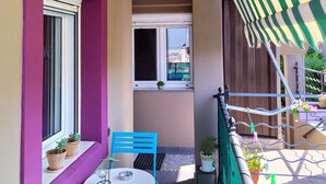 Un balcone con tavolo e sedie, una finestra e un tenda da sole a righe.