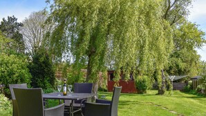 Un espace de restauration en plein air, aménagé avec des meubles en osier et une table pour deux, entouré d’une végétation luxuriante et d’arbres.
