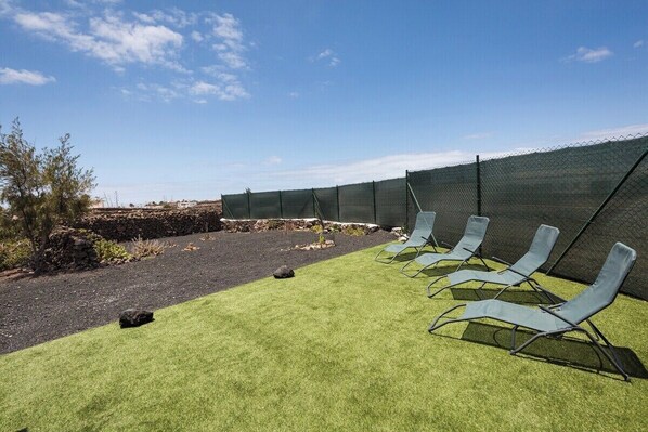 A section of a hotel with a grassy area, a stone wall, and a chain-link fence.