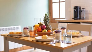 A breakfast table with croissants, fruit, and beverages in a bright room with a window and kitchen appliances in the background.