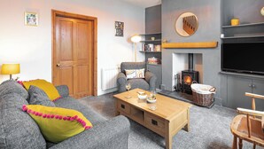 A cozy living room with a sofa, a wooden coffee table, a fireplace, a television, and a bookshelf.