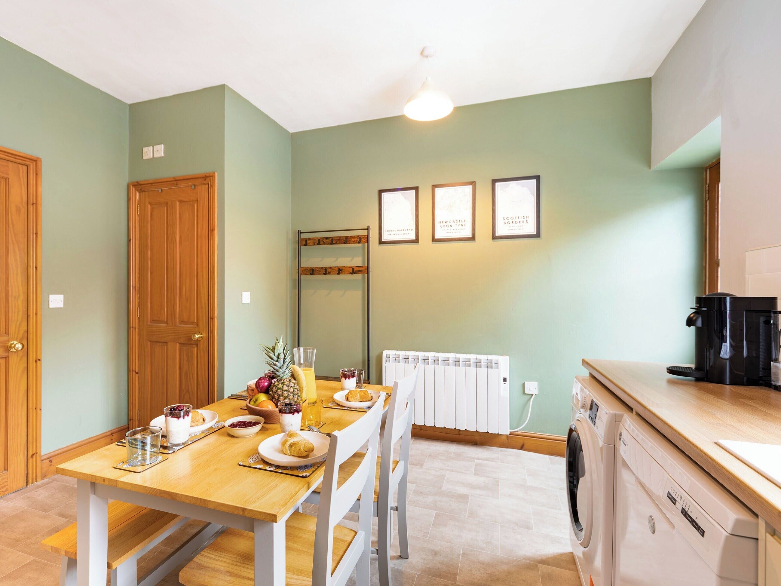 A dining area with a wooden table set for breakfast, a radiator, and a washing machine in the background.