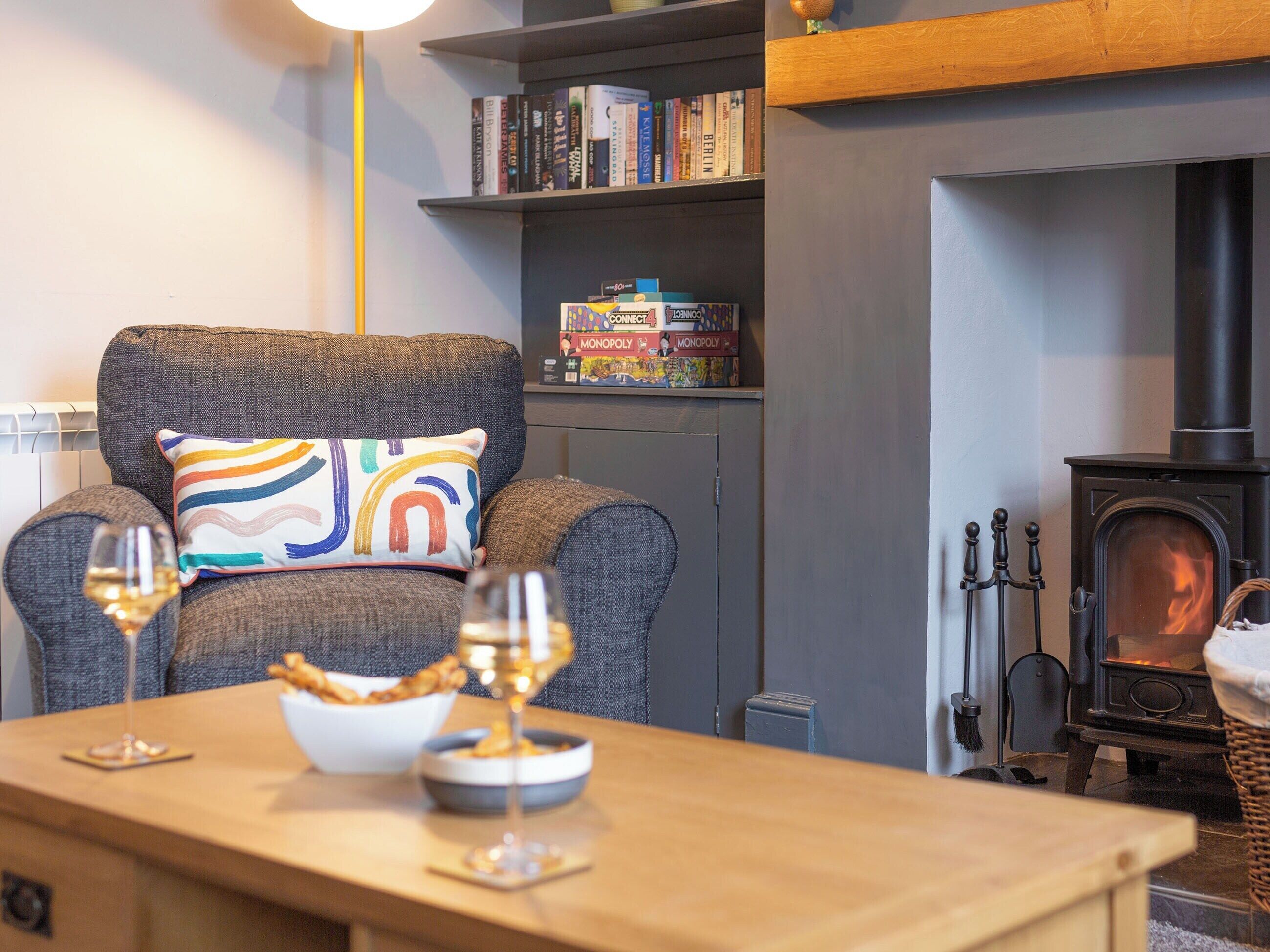 A cozy living room with a fireplace, a bookshelf, and a comfortable armchair with a colorful pillow.