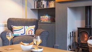A cozy living room with a fireplace, a bookshelf, and a comfortable armchair with a colorful pillow.