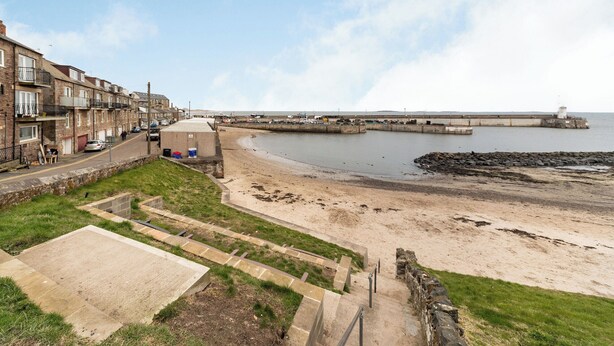 A coastal residential area with terraced houses, a sandy beach, and a sea wall.