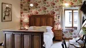 Une chambre à coucher avec un lit en bois, un papier peint à motifs floraux, une table de chevet avec des lampes et une fenêtre avec des rideaux.