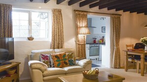A cozy living room with a sofa, a TV, a wooden coffee table, and a kitchen in the background. - 2 bedroom accommodation in Pelynt, near Looe (Pelynt, near Looe)