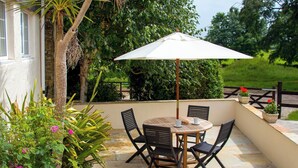 A patio with a round table and four chairs, an umbrella, and potted plants. - 2 bedroom accommodation in Pelynt, near Looe (Pelynt, near Looe)