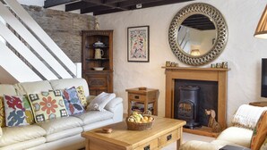 A cozy living room with a fireplace, a sofa with colorful cushions, a wooden coffee table, and a staircase with a stone wall. - 2 bedroom accommodation in Pelynt, near Looe (Pelynt, near Looe)