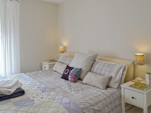 A neatly made bed with a quilt, pillows, and a bedside table with a lamp.