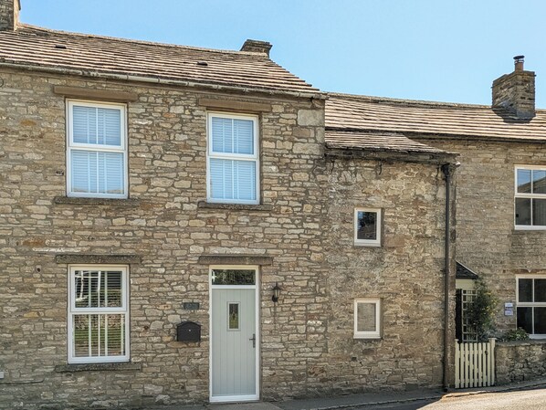 A stone building with a white door, multiple windows with shutters, and a small mailbox.