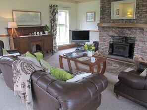 A living room with a fireplace, leather sofas, a television, and a coffee table. - Owl Cottage High Weldon (Weldon Bridge, near Rothbury)