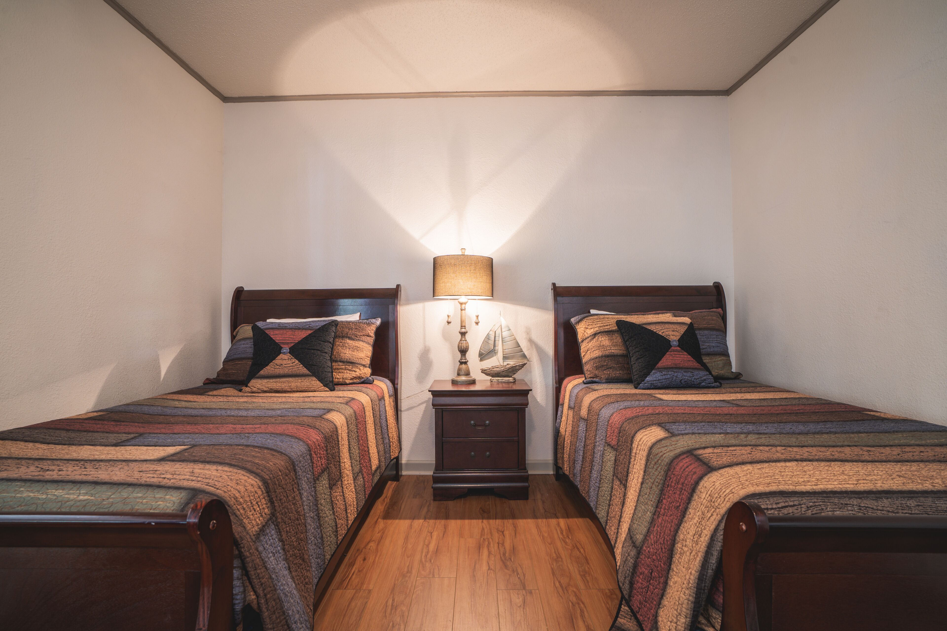 A bedroom with two single beds, a nightstand with a lamp, and a small decorative item on the nightstand.