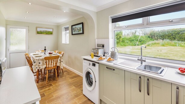 A kitchen with a washing machine, a sink, and a window with a view of greenery.