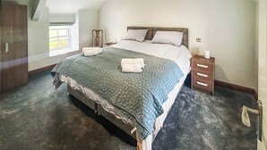 A spacious bedroom with a large bed, a wooden nightstand, and a built-in wardrobe.