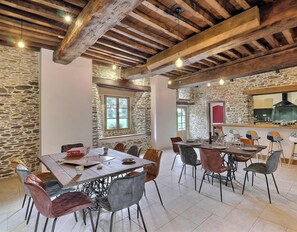 A rustic dining area with stone walls, wooden beams, and a stone fireplace.